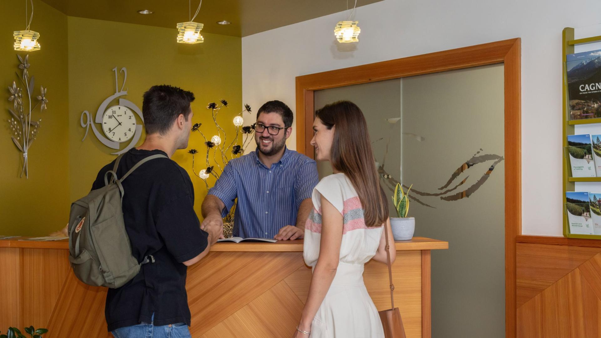 Coppia alla reception di un hotel, sorridono al receptionist.