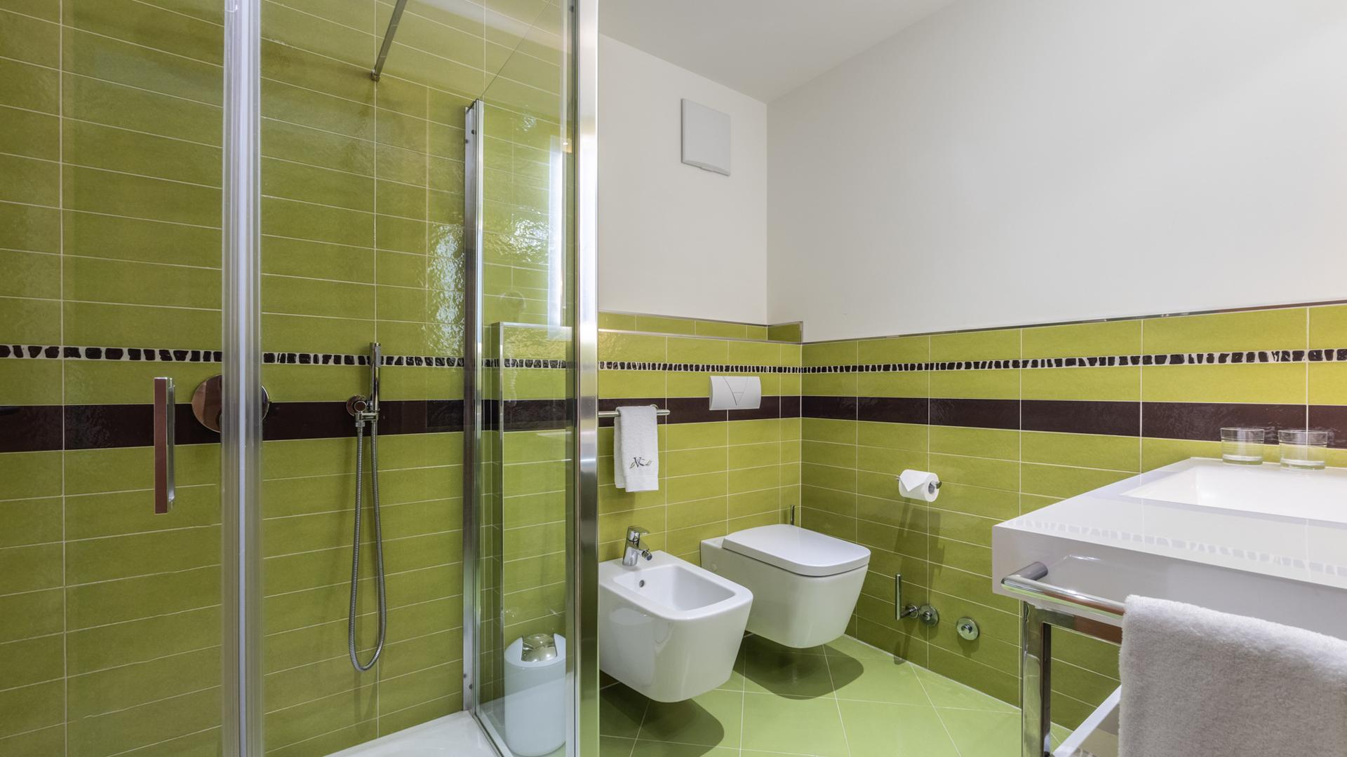 Bagno moderno con piastrelle verdi e doccia in vetro.